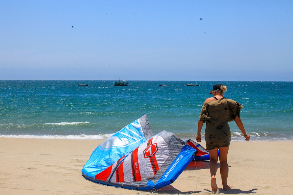 Kitesurf girl setting up her blue, red and grey kite at kitesurf beach in Peru